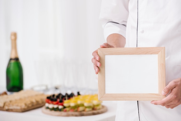 Download Chef in uniform holding wooden frame with mock-up Photo | Free Download