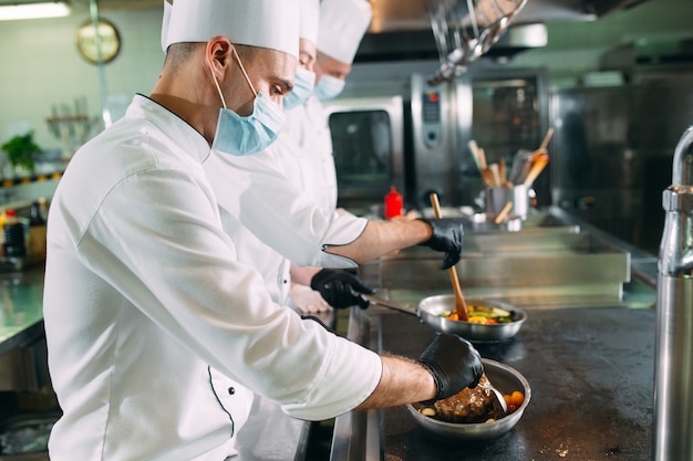 Premium Photo | Chefs in protective masks and gloves prepare food in ...