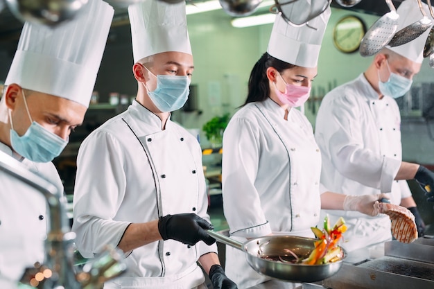 Premium Photo | Chefs in protective masks and gloves prepare food in ...