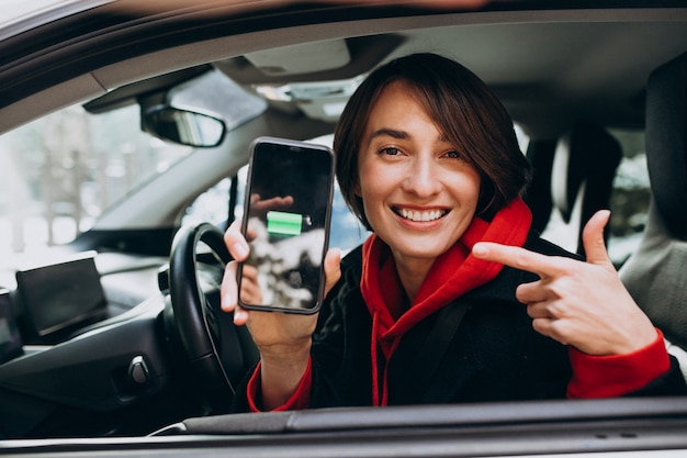 女性は彼女の車を充電し 彼女の電話でchergerを見て 無料の写真