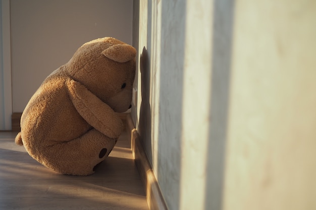 悲しみの子供の概念一人で家の壁にもたれて座っているテディベア 悲しいと失望しているように見えます プレミアム写真