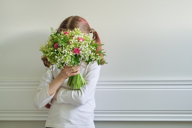 美しい春の花の花束を持つ子の女の子 花束で覆われた顔 プレミアム写真