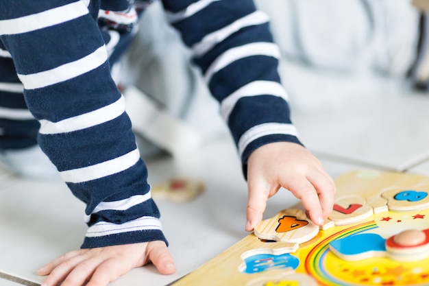 A child is playing with a wooden clock puzzle Free Photo