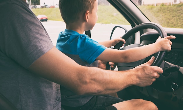 子供は車の中で父親の膝の上に座って 車の運転方法を学んでいます プレミアム写真