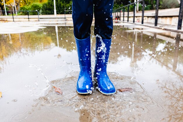 青い長靴のある公園で水たまりに子供が跳ねます プレミアム写真