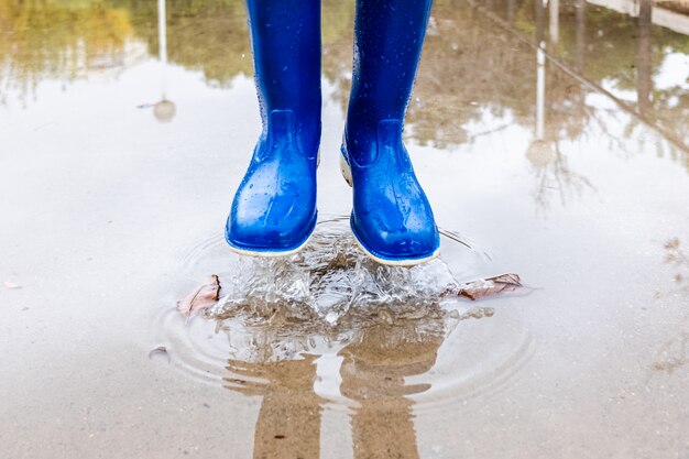 青い長靴のある公園で水たまりに子供が跳ねます プレミアム写真
