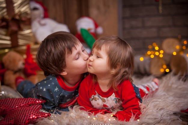 クリスマスツリーの近くの床に横たわっている子供たちの男の子と女の子は 休日の贈り物を持っています 頬に甘いキス パジャマ姿の子供たち プレミアム写真