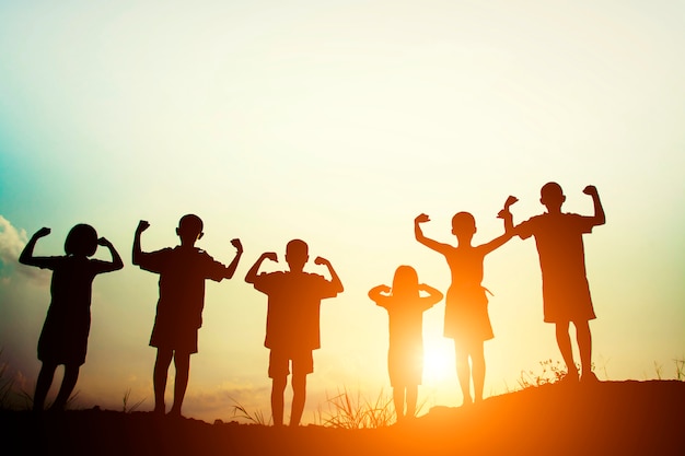 Children's silhouettes showing muscles at sunset Free Photo