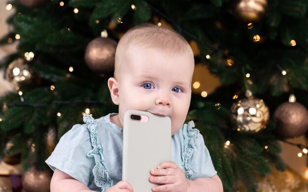 電話で話しているクリスマスの愛らしい小さな女の赤ちゃん クリスマスツリーの背景に赤ちゃんの子供の肖像画 クリスマスかわいい幼児 プレミアム写真