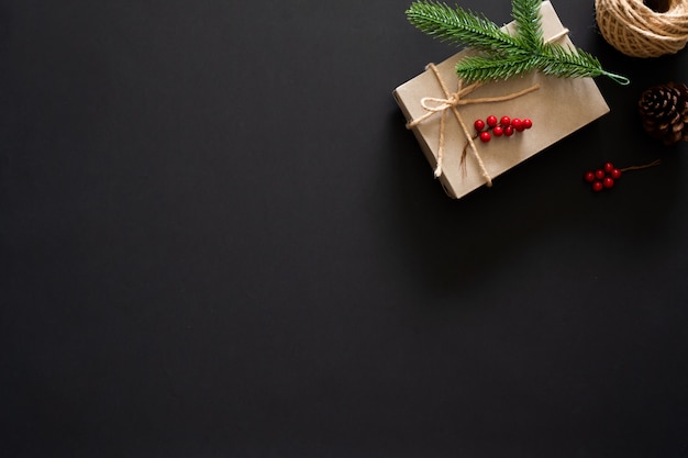 Premium Photo | Christmas gift on black background with pine branches, berries and rope