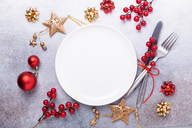 Christmas table place setting with empty white plate, cutlery with festive decorations on stone background Premium Photo