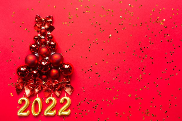  Christmas tree made of glass balls and the numbers 2022 from candles on a red background with gold 