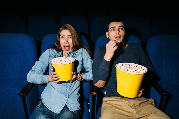 映画館でホラー映画を探しているポップコーンと若いカップル 無料の写真