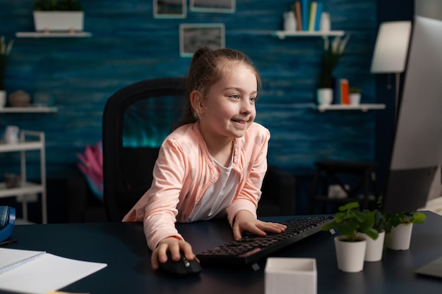 clever little schoolchild sitting at desk table using computer free photo