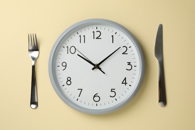 Clock, knife and fork on beige background, top view Premium Photo