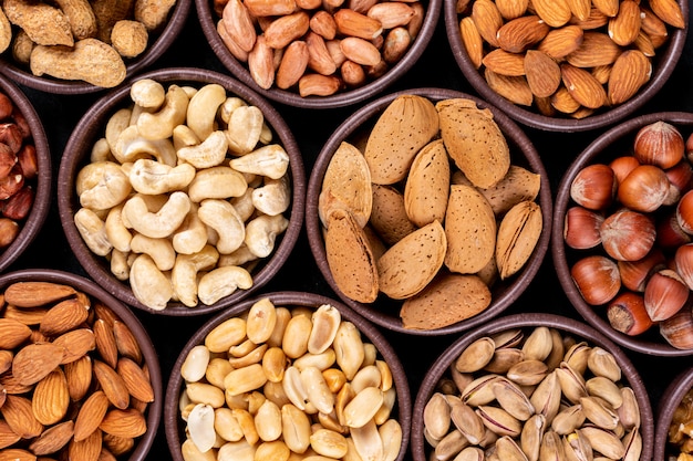 Close-up assorted nuts and dried fruits in mini different bowls with pecan, pistachios, almond, peanut, cashew, pine nuts Free Photo
