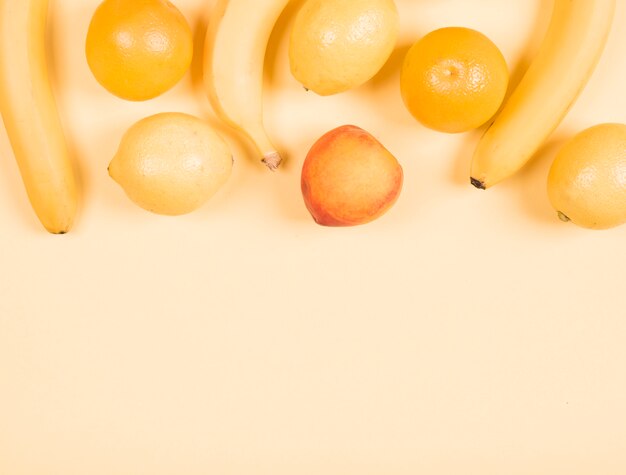 Close-up of banana; lemon; orange and peach on beige background Free Photo