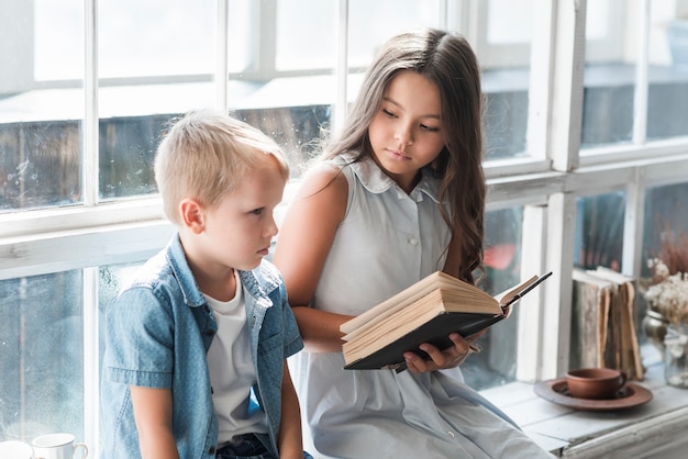 Closeup Of A Boy Sitting Near The Window Sill Reading Book Free Photo