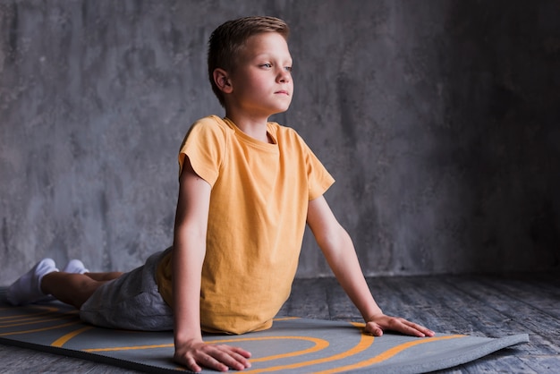 Close Up Of A Boy Stretching On Exercise Mat In Front Of Concrete