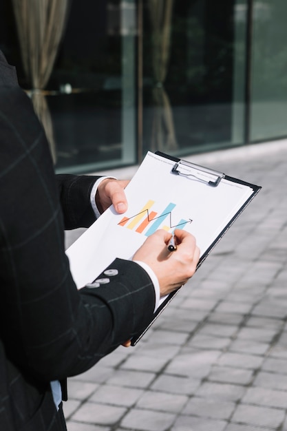 Close-up of business person's hand drawing increasing arrow on graph over the clipboard Free Photo