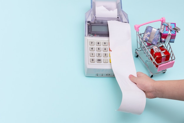 Premium Photo Close Up Of A Child S Hand Holding A Blank Cashier S Receipt Above The Cash Register Next To A Shopping Cart With Wrapped Gift Boxes