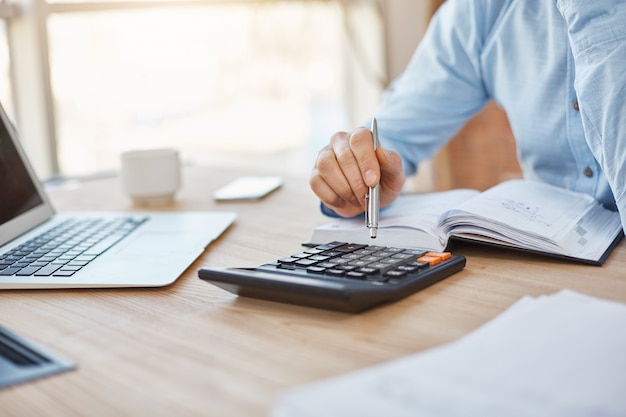 Close up detail of professional serious accountant sitting in light office, checking company finance profits on calculator Free Photo