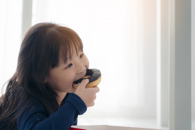 チョコレートドーナツ おいしい顔でドーナツを食べて 子供eaitngスナックを食べるかわいい子供の空腹の小さな美しいアジアの女の子の顔を閉じる プレミアム写真