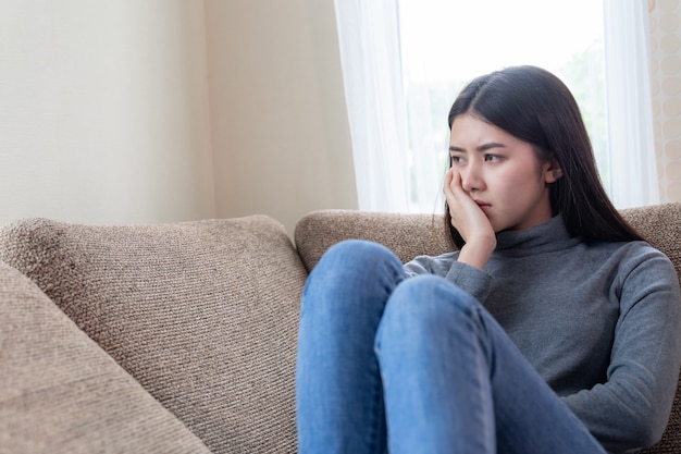 Close up face of unhappy asian pretty young woman sitting alone on couch Free Photo