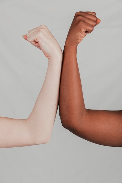 Close-up of fair and dark skinned women's hand flexing their fist against grey backdrop Free Photo
