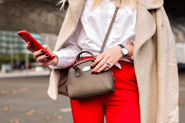 Close up fashion details you business woman , tapped something on her phone, urban autumn city background, bright suit and cashmere coat, ready for conference. Free Photo