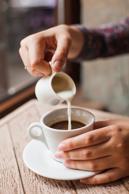 Close-up of female hand pouring milk into the coffee cup at restaurant