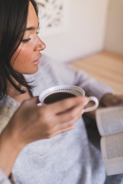 Closeup of a girl holding coffee cup reading book Free