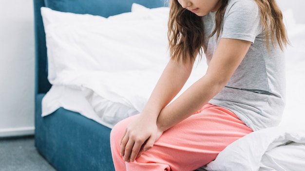 Closeup Of A Girl Sitting On Bed Touching Her Knees With Two Hands