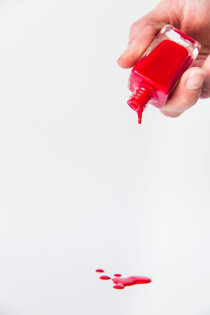 Close-up of hand pouring red nail varnish bottle on white backdrop Free Photo