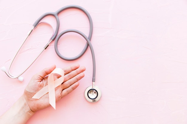 Close-up of hand showing white ribbon with stethoscope on pink backdrop Free Photo