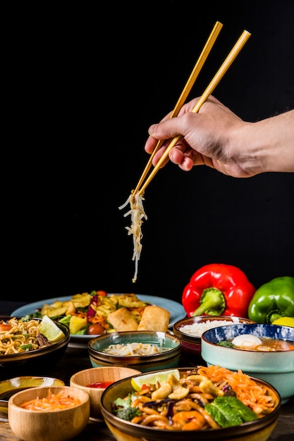 Close-up of hand using chopsticks to pick beans sprout against black background Free Photo