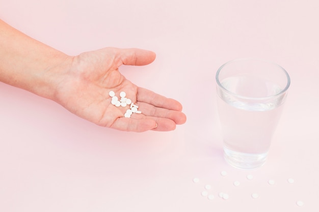 Close-up of hand with white tablets and glass of water on pink background Free Photo