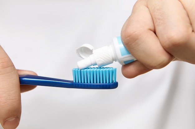 Close up image of man's hands holding tube, squeezing whitening toothpaste on brush. Free Photo