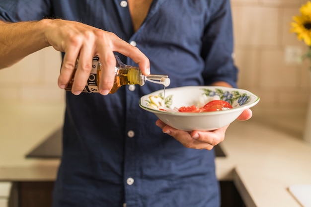 Close-up of man dressing the salad with olive oil in the bowl