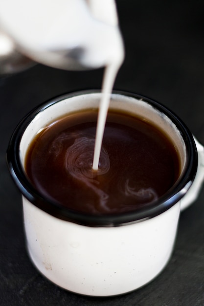 Close up milk pourred in black coffee | Free Photo