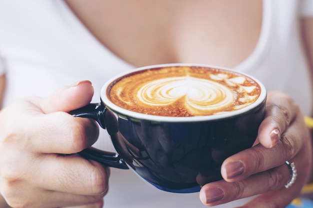 コーヒーショップカフェで女性の手にコーヒーカフェラテアートのカップのクローズアップ 無料の写真