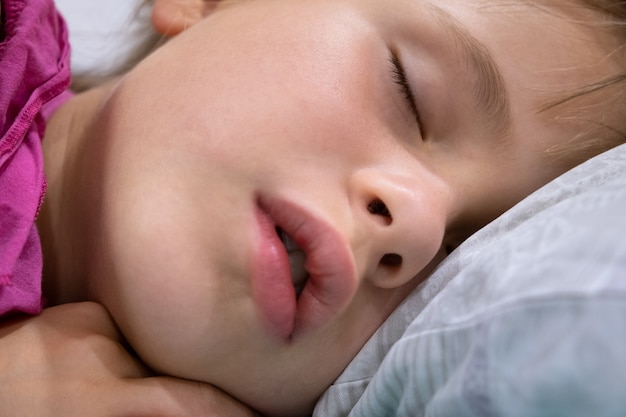 少し口を開けて 自宅のベッドで寝ている髪の周りに散らばっているかわいい子供の女の子の顔のクローズアップ プレミアム写真