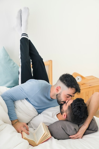 壁に彼の足でベッドに横になっているボーイフレンドにキスをする男のクローズアップ 無料の写真