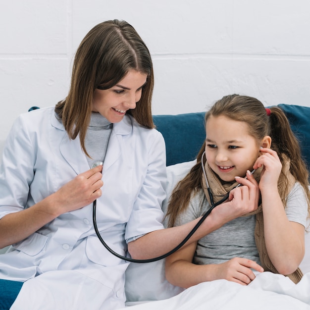 聴診器で笑顔の女性医師の心臓の鼓動を聞いて患者の女の子のクローズアップ プレミアム写真