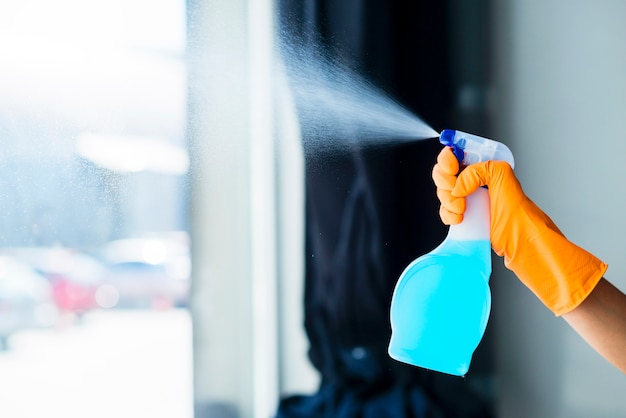 Close-up of a person's hand spraying the liquid detergent on window glass Free Photo