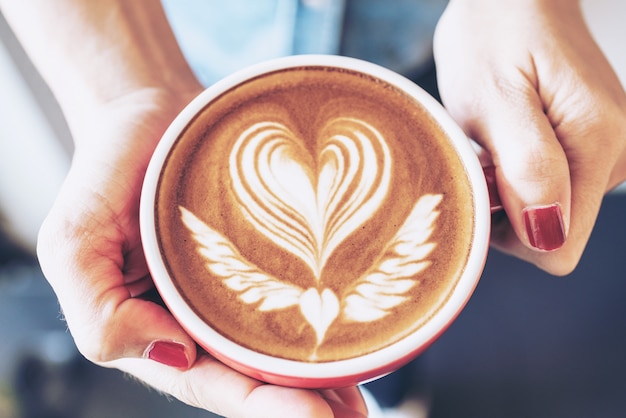 コーヒーショップカフェで女性の手にコーヒーカフェラテアートの赤カップのクローズアップ プレミアム写真