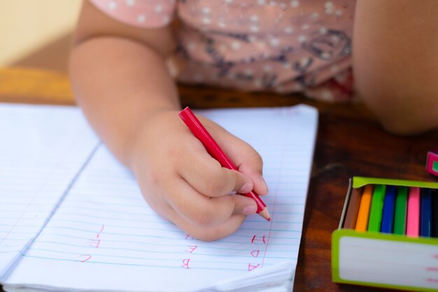 白いメモ帳の紙に手で英語の単語を書く鉛筆で女の子の手のクローズ 