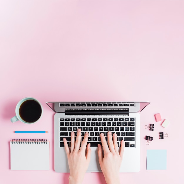 Close-up of hand typing on laptop with stationeries and coffee cup on pink backdrop Free Photo Close-up of hand typing on laptop with stationeries and coffee cup on pink backdrop Free Photo