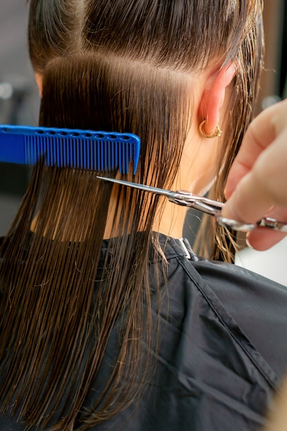 若い女性の長い髪を切る男性美容師の手のクローズアップ プレミアム写真