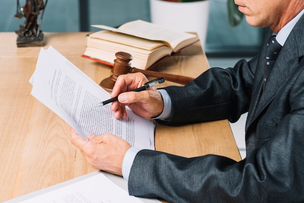 Close-up of male lawyer holding pen reading document at wooden desk Free Photo